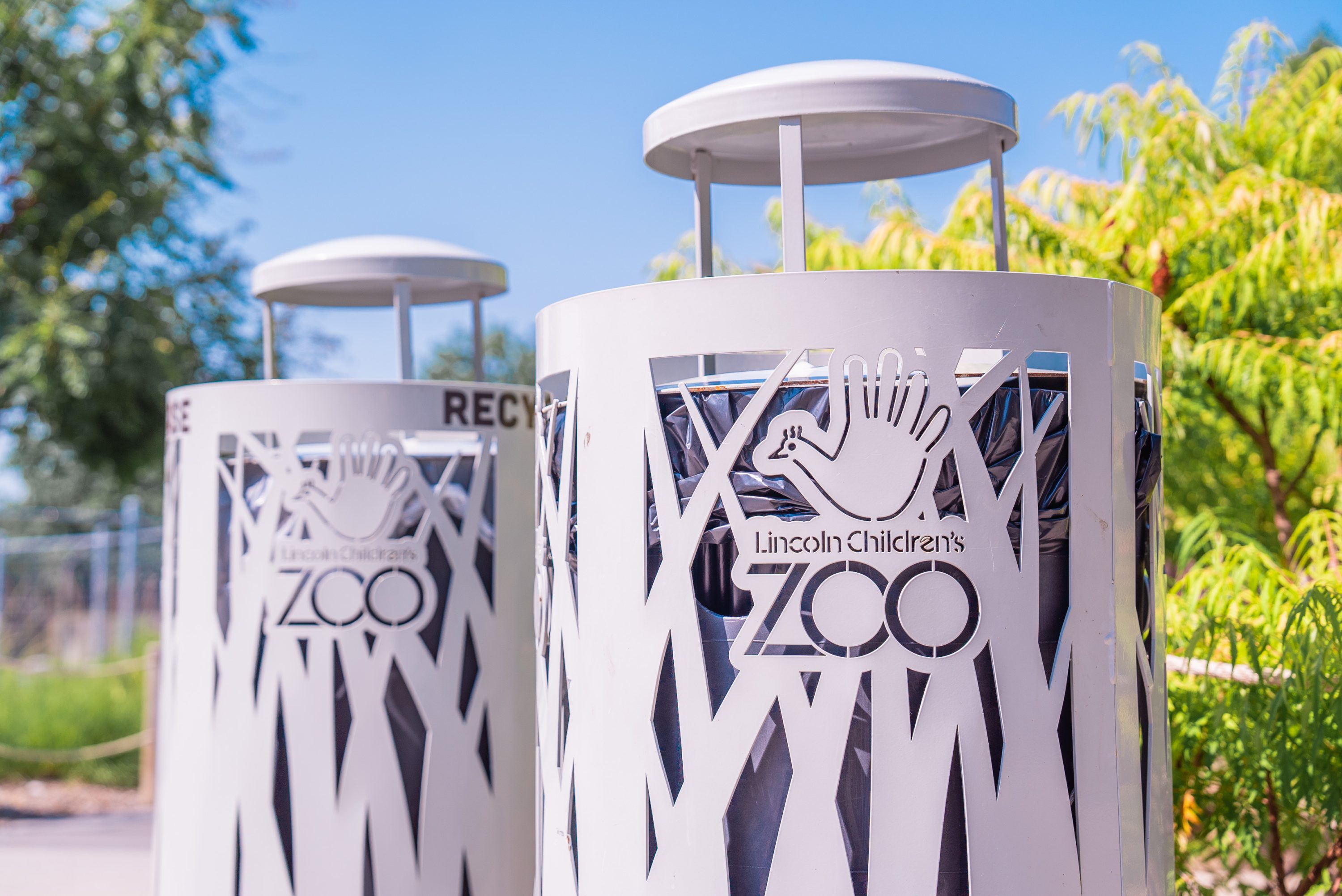 Metal trashcans with grass and the Lincoln Children's Zoo logo etched into the sides.