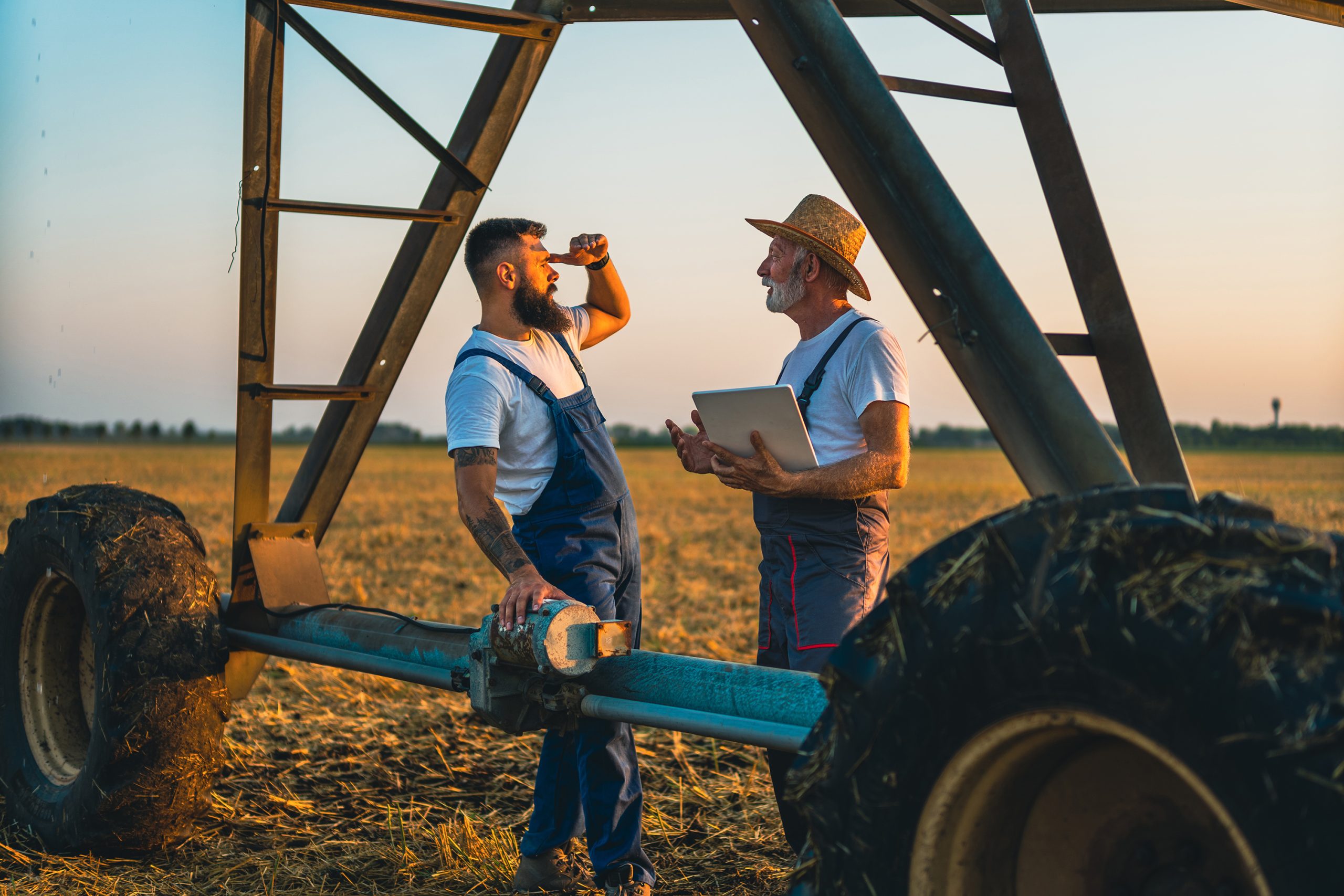 Farmers standing in field surveying. Two men next to center pivot irrigation system.